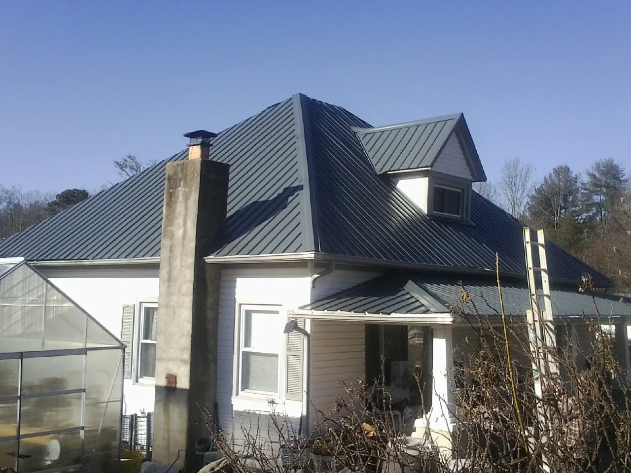 Dark blue standing seam metal roof on a white farmhouse with dormer — Slate & Tile Roof Repair by Roofing Brothers in Woodcliff Lake
