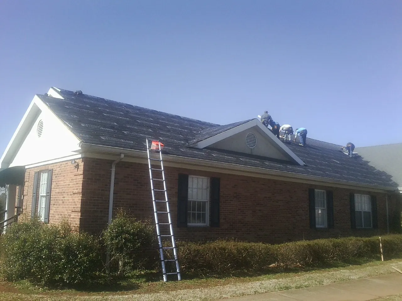 Crew tearing shingles off a brick ranch roof with a ladder set — Emergency Roof Repair work by our crew in Woodcliff Lake
