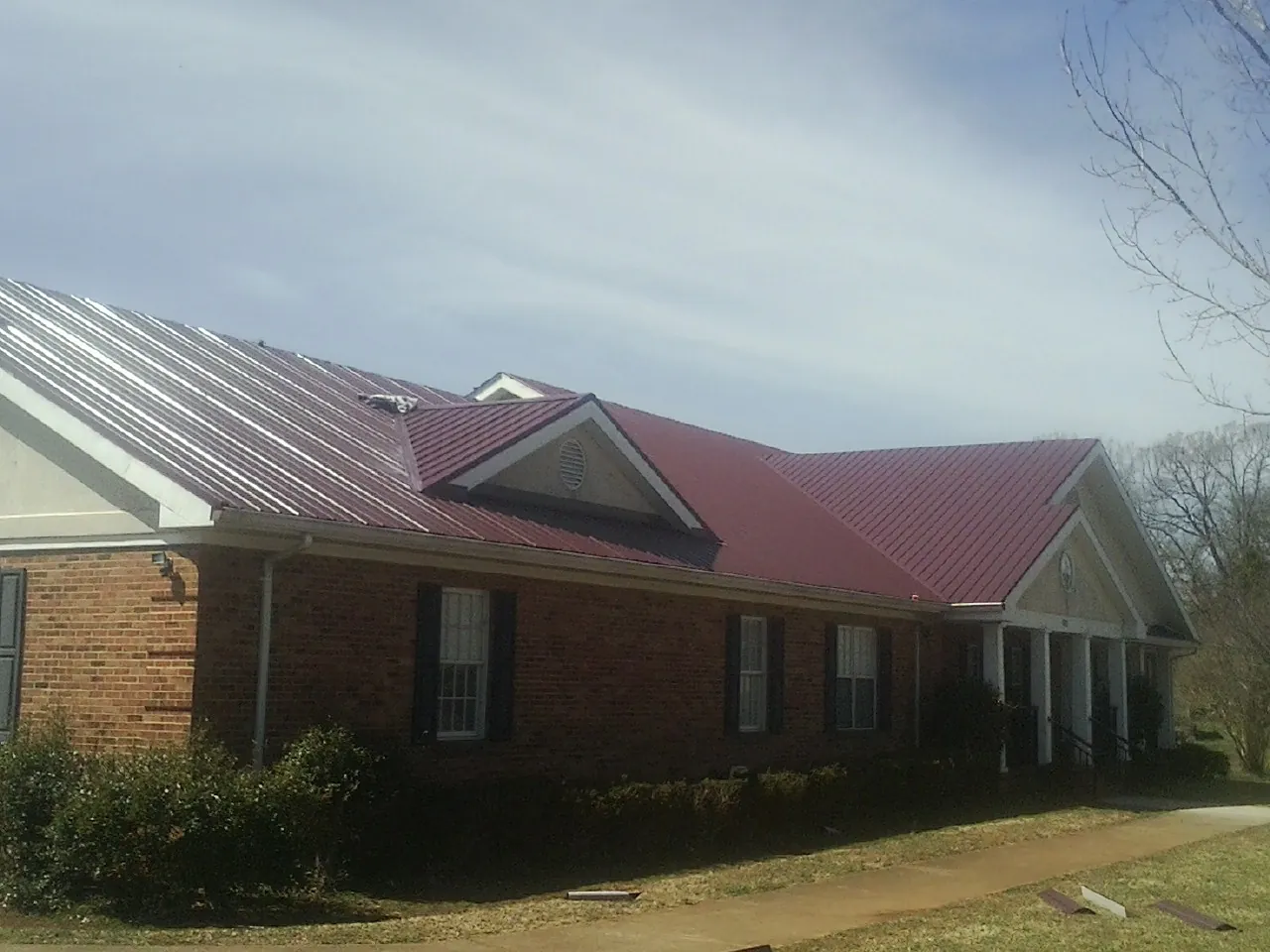 Red metal roof with gabled entries on a long brick building, from a Hail Damage Roof Repair job in Woodcliff Lake