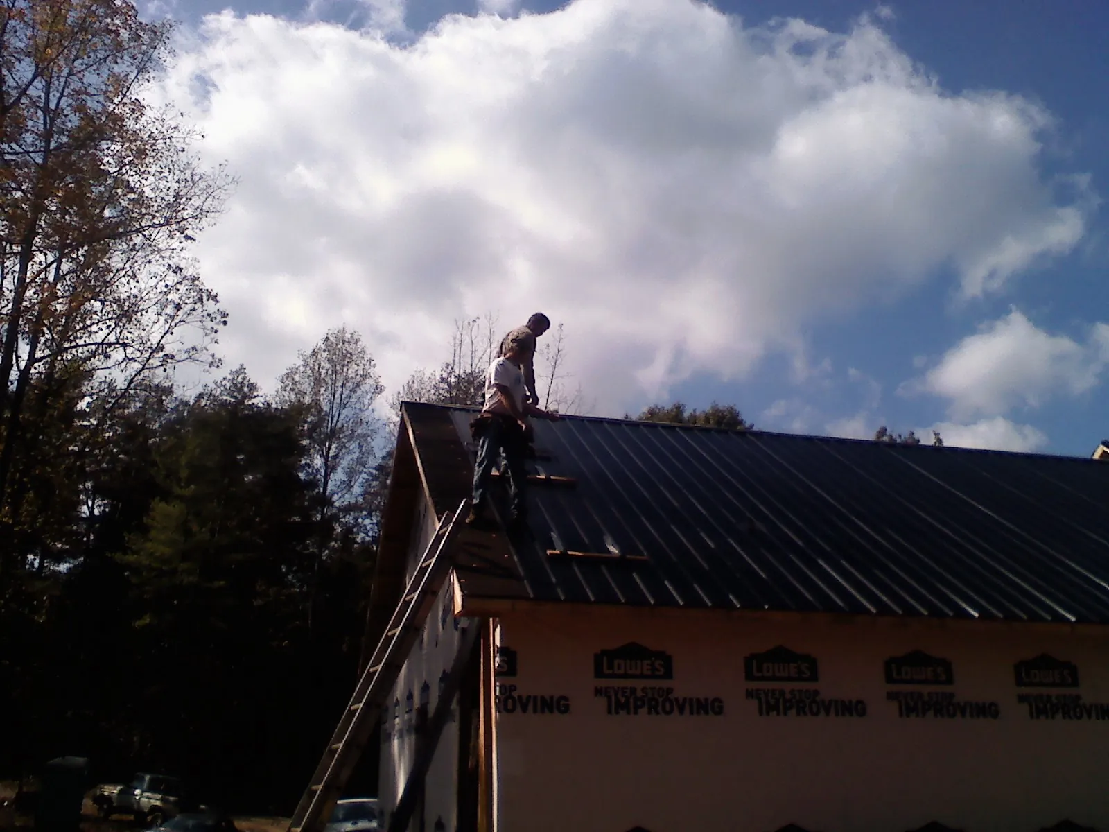 Roofer fastening dark metal panels high against a cloudy sky, from a Roof Inspection job in Woodcliff Lake