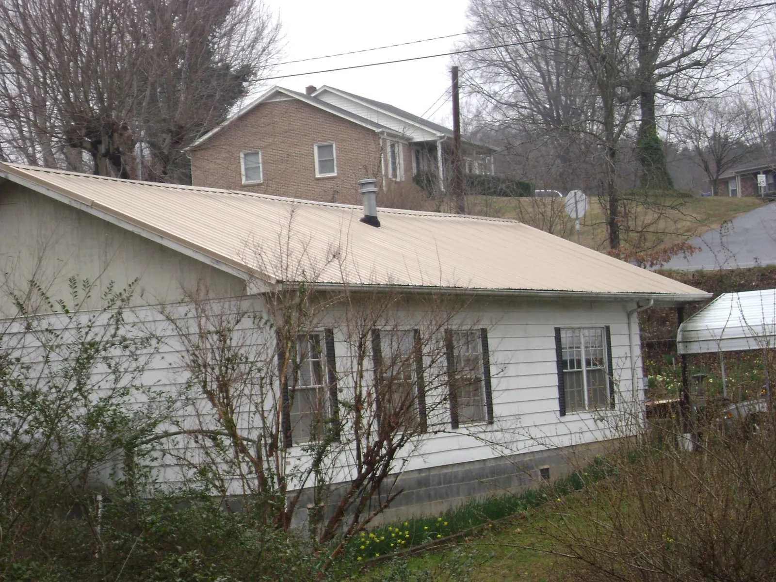 Tan metal roof on a white sided house set into a hillside — Commercial Roofing by Roofing Brothers in Woodcliff Lake